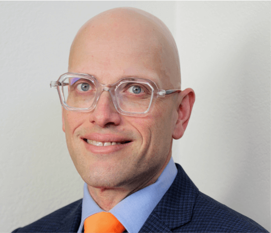 a bald man with glasses is wearing an orange tie